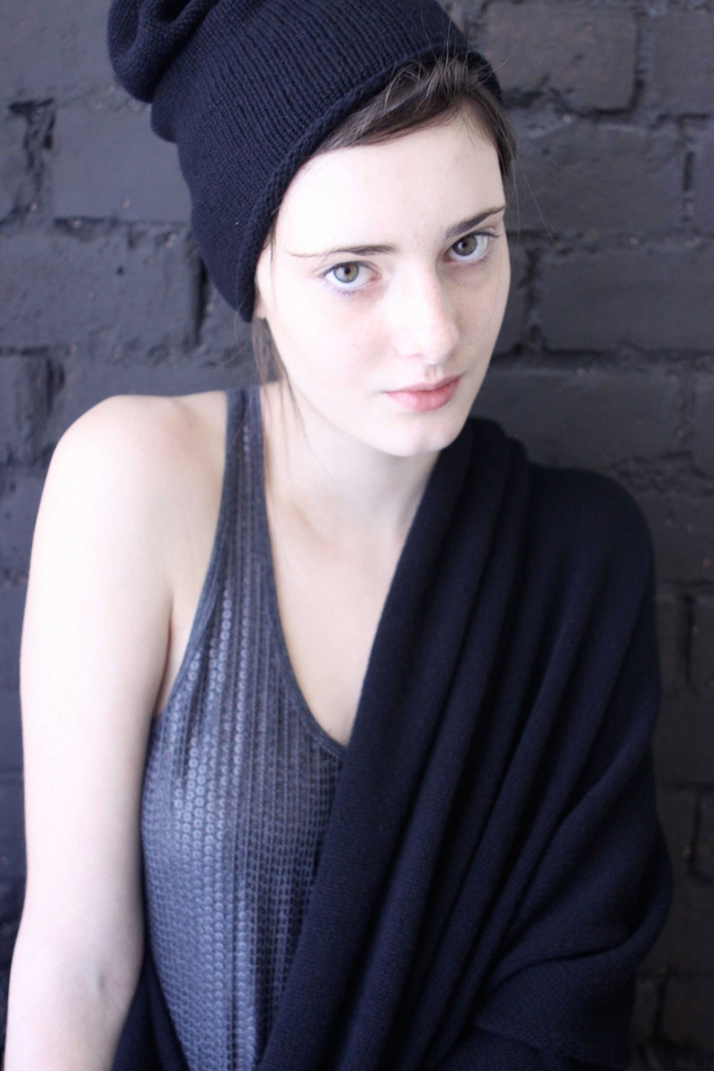 May include: A woman wearing a black knitted beanie, a grey knitted tank top, and a black knitted scarf.