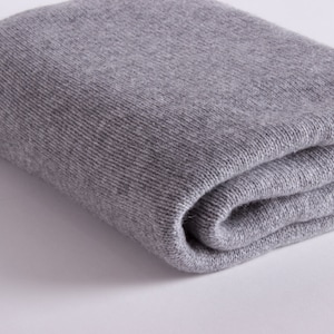 May include: A soft, grey knitted throw blanket folded on a white surface.