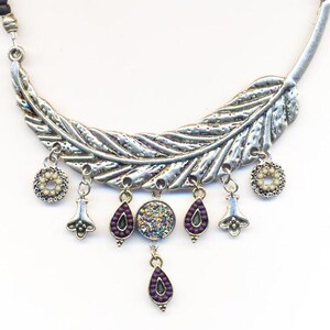 May include: Silver feather necklace with dangling charms. The charms include a round charm with iridescent glitter, teardrop charms with purple beads, and two flower-shaped charms.