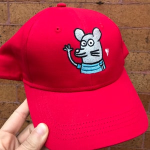 Könnte beinhalten: Rote Baseballkappe mit einer gestickten grauen Maus, die ein blaues Hemd trägt und winkt. Die Maus hat ein Herz über dem Kopf.