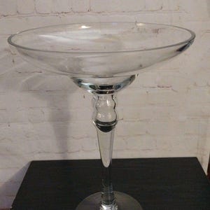 Peut inclure: Un saladier sur pied en verre transparent, avec un plat large et peu profond et une longue tige élégante. Le saladier repose sur une base circulaire. Le fond est un mur de briques blanches et une surface sombre.