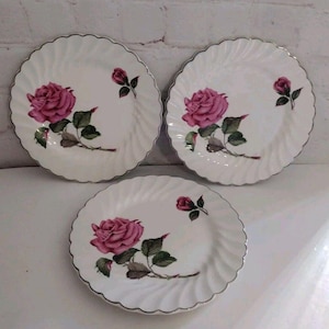 May include: Set of three white ceramic plates with a pink rose design and a silver rim.
