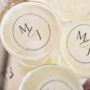 May include: Three clear glass cocktail glasses with personalized stickers. Each sticker features a black circle with the initials "M&J" and the date "08.21.2023" in white text.