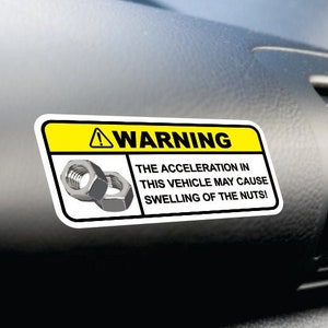 May include: A yellow and white warning sign with a black exclamation point. The sign reads "WARNING THE ACCELERATION IN THIS VEHICLE MAY CAUSE SWELLING OF THE NUTS!" and features two silver nuts.