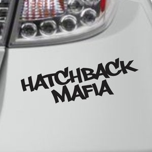 May include: A black and white vinyl sticker with the text "Hatchback Mafia" in a stylized font. The sticker is applied to the rear bumper of a silver car.
