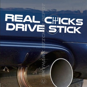 May include: White vinyl decal sticker with the text "REAL CHICKS DRIVE STICK" and a stick shift gear symbol. The sticker is on the back of a blue car.