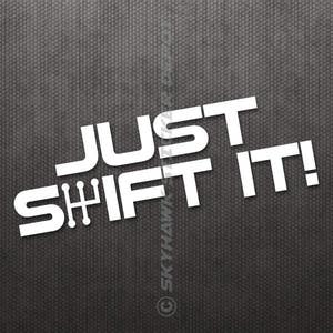Op de afbeelding: Witte vinyl sticker met de tekst "JUST SHIFT IT!" in een vet, sans-serif lettertype. De tekst is schuin geplaatst, waarbij "SHIFT" "JUST" overlapt.