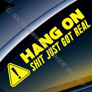 Op de afbeelding: Een geel waarschuwingsbord met een uitroepteken en de tekst "Hang On Shit Just Got Real" op een zwarte achtergrond.