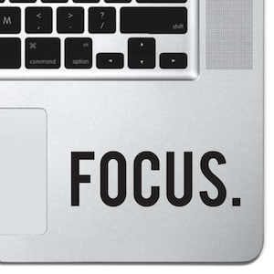 May include: A laptop keyboard with the word "FOCUS." in bold, black letters on the silver surface. The keyboard keys are black and white, with the command, option, and shift keys visible.