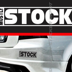 Peut inclure: Une voiture blanche avec un autocollant noir "MOSTLY STOCK" sur le pare-chocs arrière.