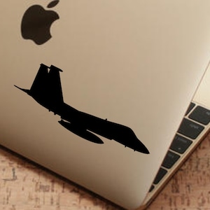 May include: A black silhouette of a fighter jet on a silver laptop computer.