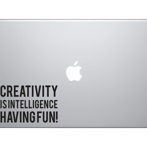 May include: A silver laptop with a white Apple logo and a black sticker that reads "CREATIVITY IS INTELLIGENCE HAVING FUN!"