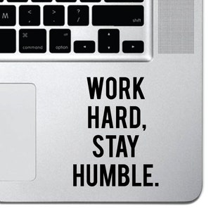 May include: A laptop computer with a black and white sticker that reads "WORK HARD, STAY HUMBLE."