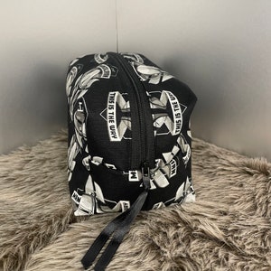 May include: Black cosmetic bag with a repeating pattern of white and gray images and the text "THIS IS THE WAY". The bag has a black zipper and a black ribbon pull.