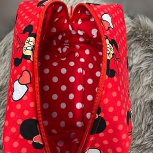 Op de afbeelding: Rode toilettas met rits, wit stippenpatroon en een Minnie Mouse-ontwerp. De tas is open en de binnenkant is gevoerd met een witte stippenstof.