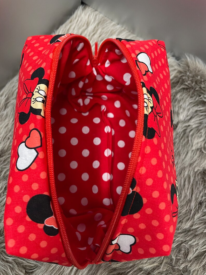Op de afbeelding: Rode toilettas met rits, wit stippenpatroon en een Minnie Mouse-ontwerp. De tas is open en de binnenkant is gevoerd met een witte stippenstof.