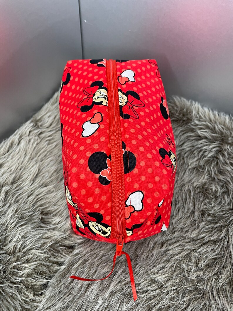 Op de afbeelding: Rode ritszak met een stippenpatroon en een Minnie Mouse-print. De tas heeft een rode rits.