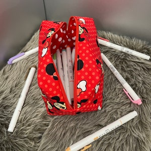 Op de afbeelding: Rode rits-pennenkoker met een stippenpatroon en een Minnie Mouse-ontwerp. De koker is open en gevuld met kleurrijke stiften.