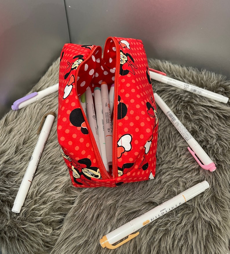 Op de afbeelding: Rode rits-pennenkoker met een stippenpatroon en een Minnie Mouse-ontwerp. De koker is open en gevuld met kleurrijke stiften.