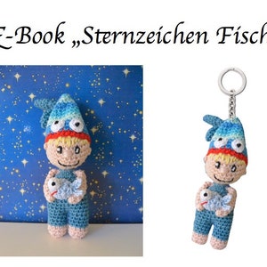 Op de afbeelding: Gehaakte pop met een blauw-witte hoed, die een vis vasthoudt. De pop heeft een lachend gezicht, rood haar en een blauwe overall. De afbeelding bevat de tekst "E-Book Sternzeichen Fische".