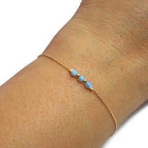 Peut inclure: Un bracelet délicat en chaîne dorée avec trois petites perles d'opale bleues.