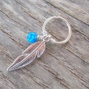Könnte beinhalten: Ein silberner Creolenohrring mit einem blauen Opal-Perlen und einem silbernen Feder-Anhänger.