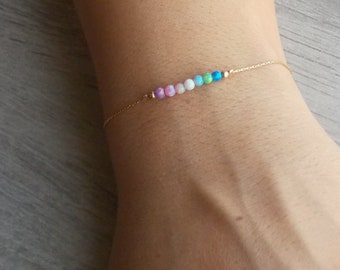 May include: A delicate gold chain bracelet with a row of colorful opal beads. The beads are arranged in a gradient from purple to blue.