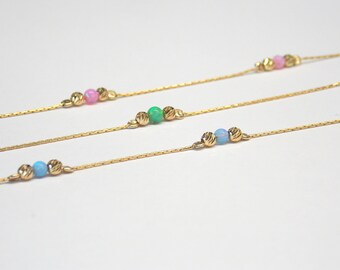 May include: Three gold chains with different colored beads. The top chain has pink beads, the middle chain has green beads, and the bottom chain has blue beads.