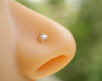 May include: A gold nose ring with a small white pearl in the center.
