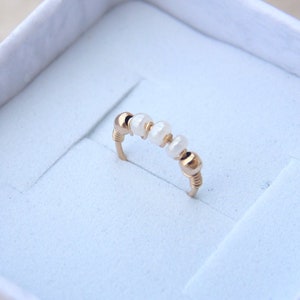 Può includere: Un delicato anello d'oro con piccole perle bianche, presentato in una scatola bianca.