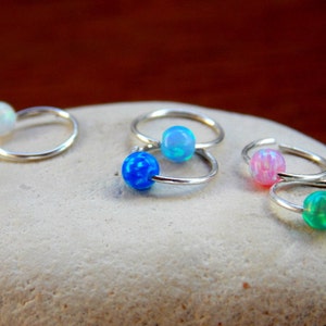 Può includere: Cinque orecchini a cerchio d'argento con pietre preziose di opale. I cerchi sono piccoli e delicati. Gli opali sono in tonalità di blu, verde, rosa e bianco.