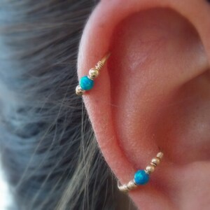 Puede incluir: Aretes de aro de oro con cuentas de &oacute;palo turquesa. Los aretes se llevan en el cart&iacute;lago superior de la oreja.