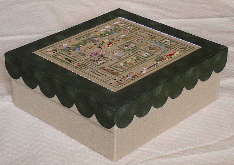 May include: A green and beige box with a scalloped edge and a stitched design of a spring scene with the word "Spring" in the centre.