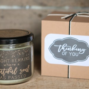 May include: A glass jar candle with a black lid and a label that reads "A light remains where a beautiful soul has passed". The candle is packaged in a brown box with a white sticker that reads "Thinking of you".
