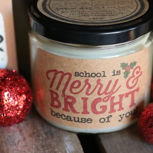 May include: A brown candle jar with a white label that reads "school is Merry & BRIGHT because of you". The candle jar is surrounded by red glitter ornaments.
