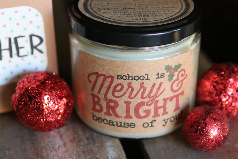 May include: A brown candle jar with a white label that reads "school is Merry & BRIGHT because of you". The candle jar is surrounded by red glitter ornaments.
