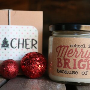 May include: A brown box with the word "TEACHER" on it, a jar of candle with a brown label that says "school is Merry & BRIGHT because of you!" and three red glitter ornaments.