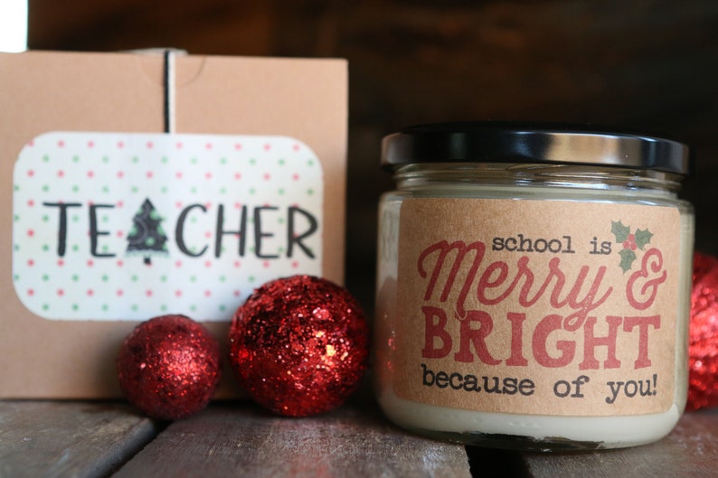 May include: A brown box with the word "TEACHER" on it, a jar of candle with a brown label that says "school is Merry & BRIGHT because of you!" and three red glitter ornaments.