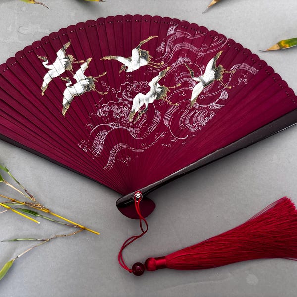 Abanico de mano de bambú color granate: Grullas y arte dorado. Incluye bolsa de regalo.