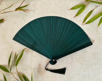 May include: A dark green hand fan made of bamboo with a decorative tassel. The fan is closed and has a delicate, intricate design.