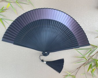 May include: A black and purple hand fan with a black tassel. The fan is made of silk and has a delicate design.