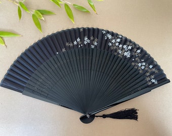 May include: A black folding fan with a white floral design and a black tassel. The fan is made of wood and has a delicate, intricate design.