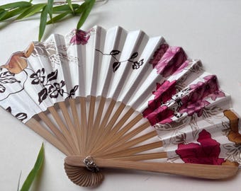 May include: A white and pink folding hand fan with a floral design. The fan is made of paper and bamboo.