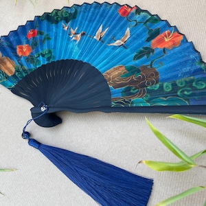 Puede incluir: Un abanico azul y negro con un dise&ntilde;o floral y de p&aacute;jaros. El abanico tiene un borla azul.