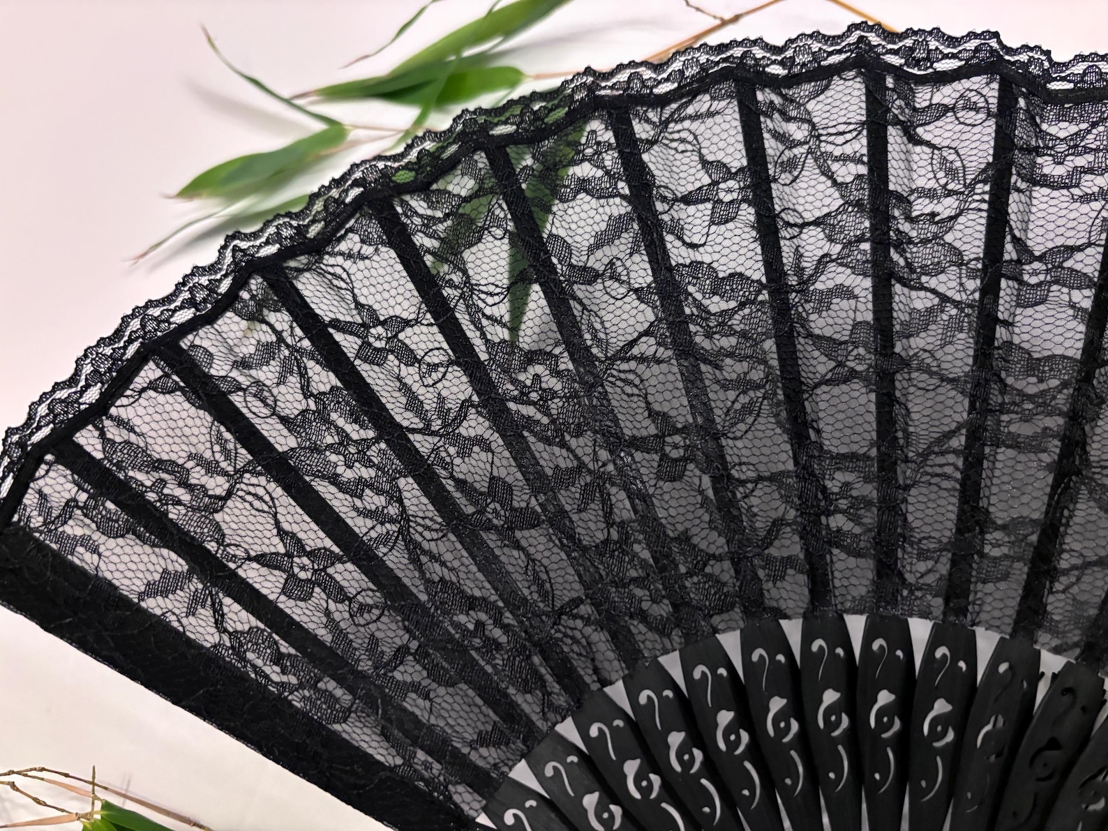 Close-up of gothic black lace folding fan with floral pattern and carved black ribs, shown partially open on a white background.