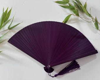 May include: A purple folding fan with a tassel. The fan is made of wood and has a delicate, intricate design.