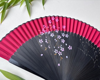 May include: A black and red folding fan with a cherry blossom design. The fan is closed and has a red fabric covering the top half. The bottom half is black with a white cherry blossom design.