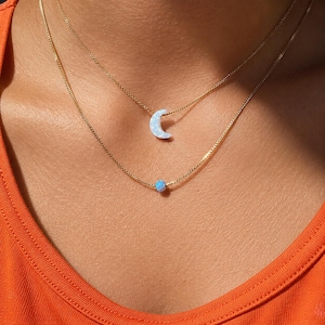 Lucky Charms USA layered necklace worn on skin featuring a light blue opal moon pendant and delicate blue opal accent on 14k gold-filled chain, designed for everyday wear with a refined lightweight feel and elevated craftsmanship.