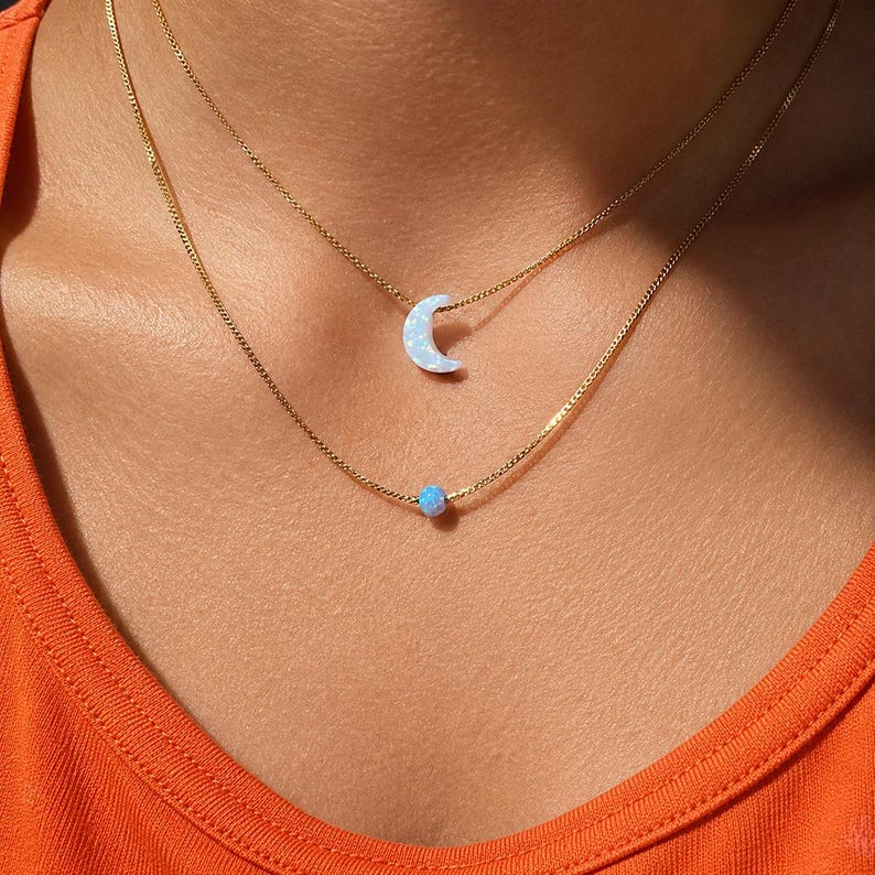 Lucky Charms USA layered necklace worn on skin featuring a light blue opal moon pendant and delicate blue opal accent on 14k gold-filled chain, designed for everyday wear with a refined lightweight feel and elevated craftsmanship.