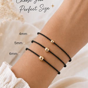 Black cord bracelet size comparison showing 4mm, 5mm and 6mm gold ball options stacked on a woman's wrist, adjustable waterproof minimalist bracelet handmade by Lucky Charms USA